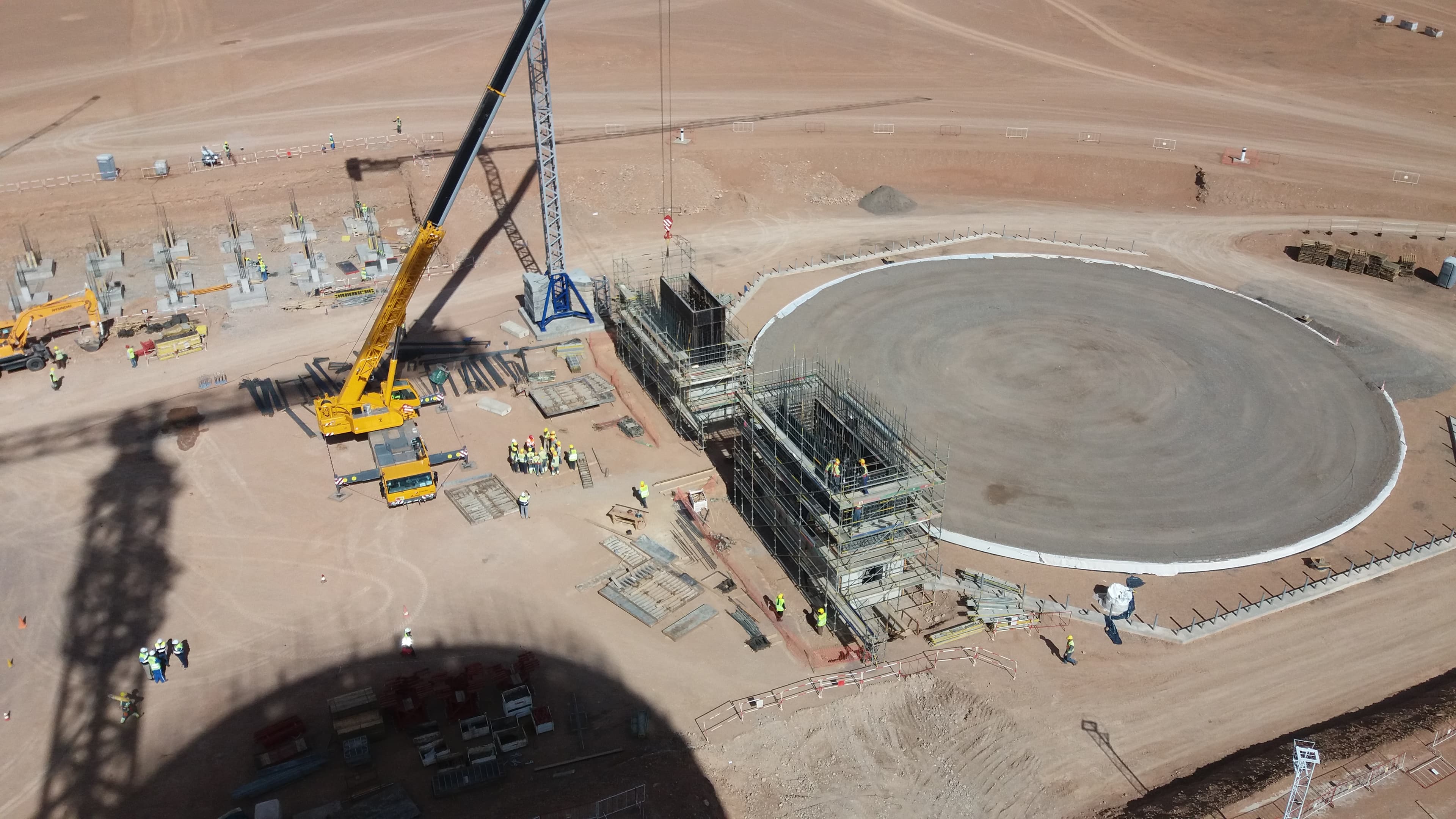 Grue jaune et ouvriers travaillant sur une grande fondation circulaire dans un désert.