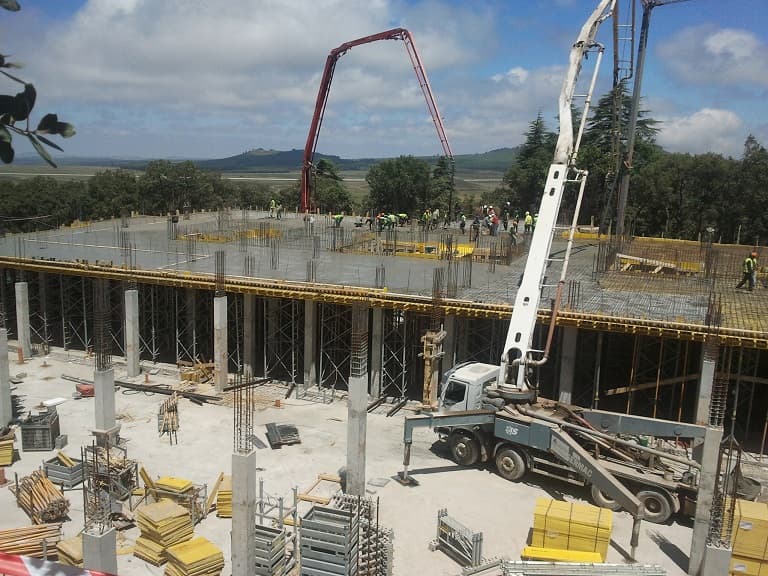 Chantier de construction avec deux camions-pompes versant du béton sur une dalle en hauteur.