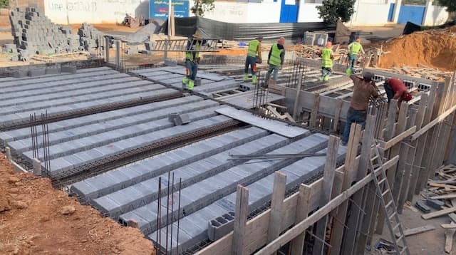 Des ouvriers du bâtiment posent des blocs de béton sur une armature en fer.