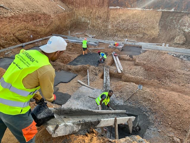 Ouvriers en gilets de sécurité coulant du béton dans les fondations d'un chantier d'excavation.