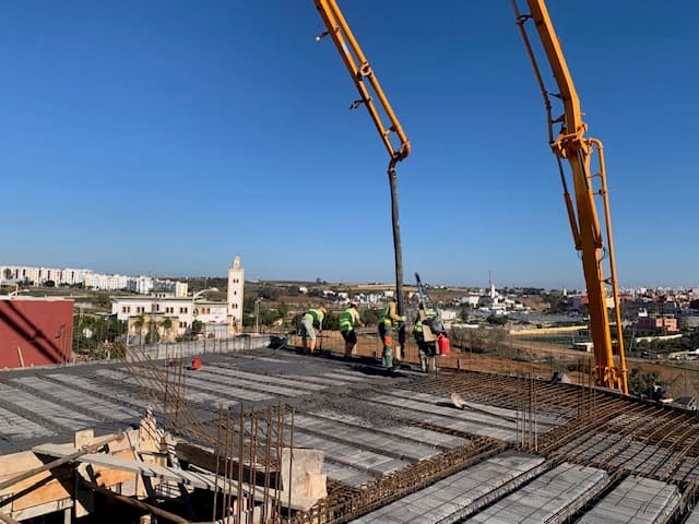Ouvriers utilisant une pompe jaune pour couler du béton sur un toit en construction.