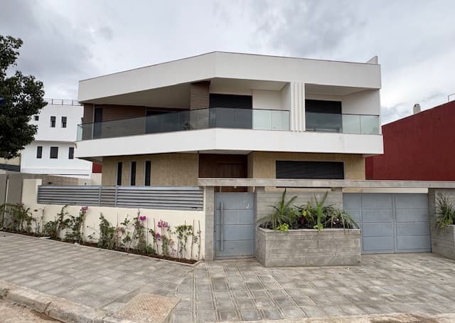 Villa contemporaine blanche et beige avec balcon vitré, portail gris et trottoir pavé devant.
