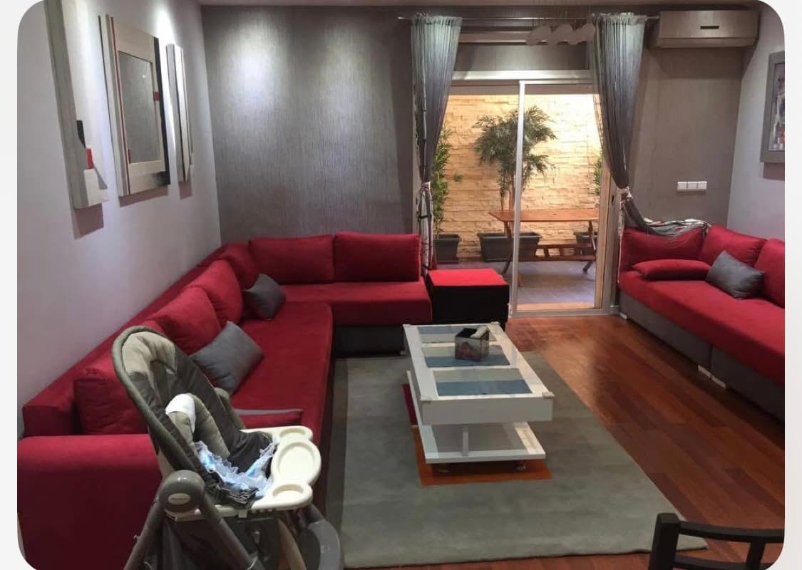 Salon moderne avec canapés rouges, table basse blanche et vue sur un patio extérieur.